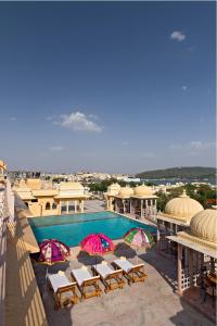 a pool with chairs and umbrellas on top of a building at Chunda Palace in Udaipur
