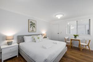 a white bedroom with a bed and a table at Sea Pine Studio in Sawtell