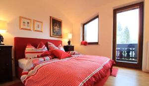 a bedroom with a bed with a red comforter and two windows at Enzian 14 - Schmuckstück von Bad Kleinkirchheim in Bad Kleinkirchheim