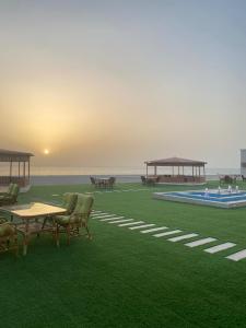 um campo verde com cadeiras e mesas e o oceano em Hotel Danat Al Khaleej em Ḩilf