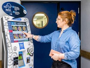 a woman pointing to a vending machine in a room at ibis budget Paris Porte d'Italie Ouest in Le Kremlin-Bicêtre