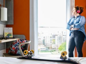 a woman standing in front of a window with a skateboard at ibis budget Paris Porte d'Italie Ouest in Le Kremlin-Bicêtre
