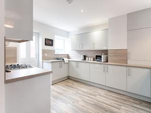 a kitchen with white cabinets and a wooden floor at Pass the Keys Luxury Bright Spacious Family Home - Near Beaches in Swansea
