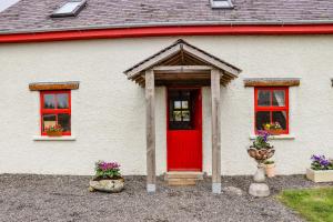 a white house with a red door and two windows at Cob Cottage in Tomhaggard