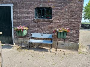 a bench and two flower pots in front of a brick wall at Het Voorhuis boerderij Hoeve Vrede Best in Weesp