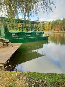 a green boat sitting on the water next to a dock at le bateau sur lac privé de 2 hectares poissonneux au milieu des bois in Florennes