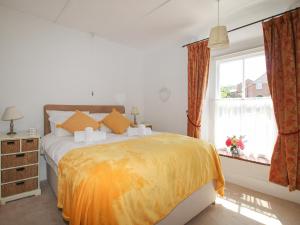 a bedroom with a bed with an orange blanket and a window at Poppy Cottage in Swanage