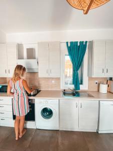a woman standing in a kitchen with a washing machine at Αλός αήρ suites in Kithnos +5 photos