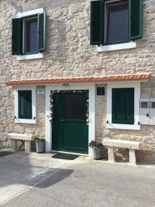 a stone building with a green door and two benches at Stein Haus in Pirovac