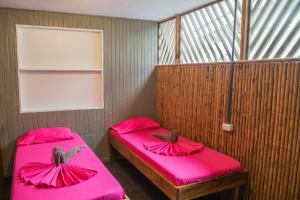 two beds in a room with pink sheets at Roots Family in Puerto Viejo