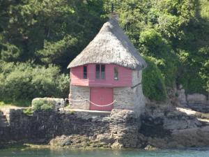 a small house with a thatched roof on the water at The Sloop Inn in Kingsbridge