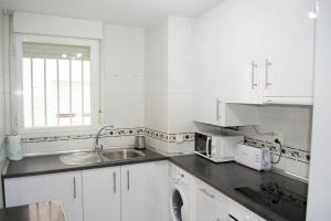 biała kuchnia ze zlewem i oknem w obiekcie Apartamenticos Torrenueva I w Saragossie