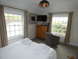 a bedroom with a bed and a chair and two windows at The Sloop Inn in Kingsbridge