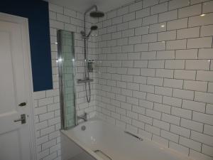 a white tiled bathroom with a tub and a mirror at The Sloop Inn in Kingsbridge