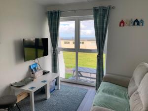 a living room with a couch and a tv and a window at Chalet 26 Widemouth Bay in Bude