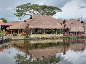 a house with a thatched roof next to a body of water at Hotel Campestre San Joaquin in Garzón