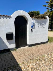 a white building with a black door and a wall at Cliff top Garden room in Milford on Sea