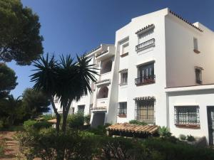 a white building with a palm tree in front of it at Apartment with amazing seeview in Miraflores Monte B in La Cala de Mijas