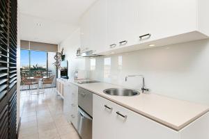 a white kitchen with a sink and a table at 128 Santai - Stylish Resort Apartment by uHoliday in Casuarina