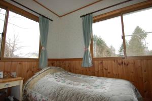 a bedroom with a bed and two windows at ヴィラコテージ Chaconne Karuizawa in Karuizawa