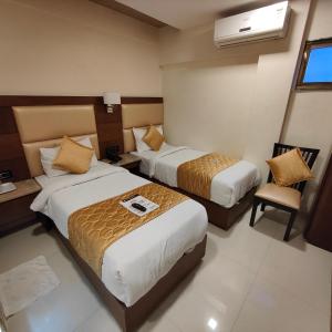 a hotel room with two beds and a chair at Oxford Hotel Powai in Mumbai
