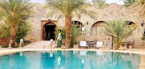 a woman standing in front of a building with a swimming pool at AUBERGE KSAR MERZOUGA in Merzouga