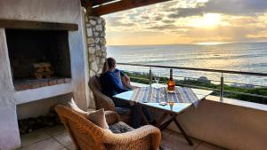 a woman sitting at a table on a balcony overlooking the ocean at Kleinzee Oceanfront Guesthouse in Gansbaai