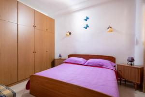 Thodoros apartment في سيكيا: غرفة نوم مع سرير مع أوراق أرجوانية ودواليب خشبية