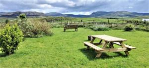 una mesa de picnic y un banco en un campo de hierba en Donmar Cottage en Skeabost