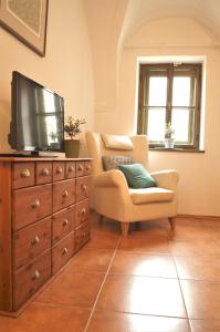 a living room with a television and a dresser with a chair at Olivea penzion & wine Mikulov in Mikulov