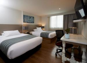 a hotel room with two beds and a desk at Hotel Saint Simon in Bogotá