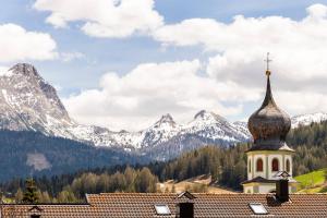 a church with a tower with mountains in the background at Residence Bosco Verde in San Cassiano