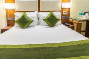 a large white bed with two green pillows on it at Super Inn Armoise Hotel in Ahmedabad