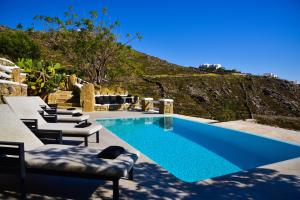 a blue swimming pool with chairs and a hill at VILLA AGNES MYKONOS in Mikonos