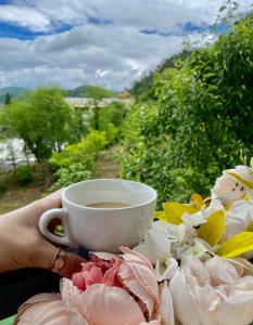 a person holding a cup of coffee next to flowers at Aloft House in Kutaisi