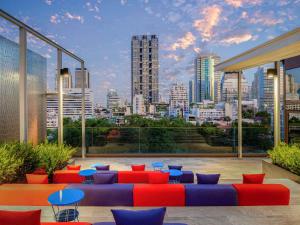 バンコクにあるibis Styles Bangkok Silomの赤と青の家具と街のスカイラインが備わる屋上パティオ