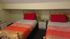 two beds with red pillows in a bedroom at Park House B&B in Leeds