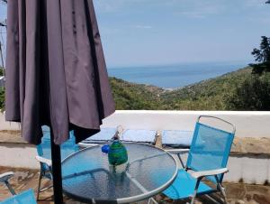 a glass table and two chairs and an umbrella at Blue Vista Ikaria in Arethousa