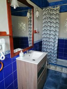 y baño con lavabo, espejo y azulejos azules. en Hostería Casa Flor, en Murias de Rechivaldo