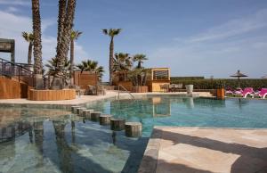 a swimming pool with palm trees in a resort at Grand Hôtel Les Flamants Roses Thalasso & Spa in Canet-en-Roussillon