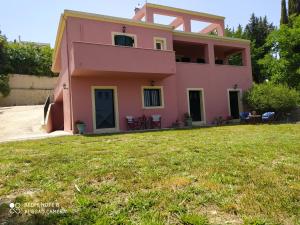 Corfu Villa Galini في Potamós: منزل وردي مع حديقة أمامه