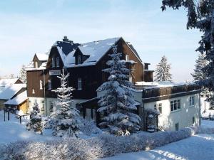 une grande maison avec des arbres enneigés devant elle dans l'établissement Gasthaus Kobär, à Kurort Altenberg