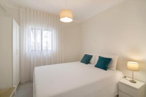 ein weißes Schlafzimmer mit einem weißen Bett und blauen Kissen in der Unterkunft Apartamento Jardins da Falésia in Albufeira