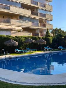a swimming pool with chairs and umbrellas next to a building at Comfy apartment in the heart of the Costa del Sol in Mijas Costa