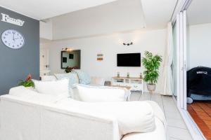 a living room with white furniture and a clock on the wall at Ocean Blue at Chakas Cove, Beachfront Apartment in Ballito