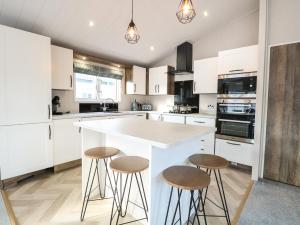 una cocina con armarios blancos y una isla con taburetes en Broadland Sands Lodge, en Lowestoft