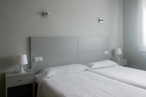 1 dormitorio con 1 cama con sábanas blancas y 2 lámparas en Apartamentos Angelito en Playa América