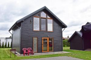 a black house with two red chairs in front of it at Kotedžai GULBĖS TAKAS Šventojoje in Šventoji