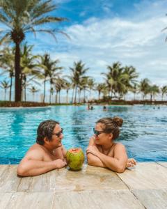 a man and a woman sitting in a pool with a coconut at Golf Ville Resort Brisa do Golf -Apartamentos e Cobertura in Aquiraz