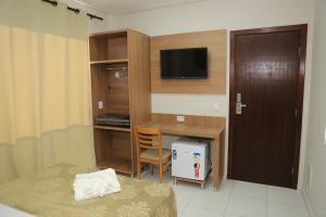 Habitación pequeña con escritorio, cama y TV. en Pontal Executive Hotel en Curvelo